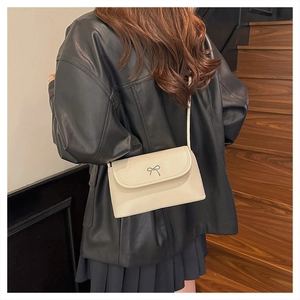 Détail du sac beige avec nœud en métal argenté et rabat porté par le mannequin
