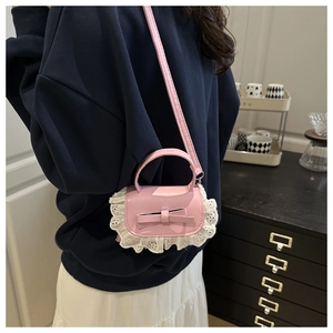 Pink mini crossbody bag with delicate lace trim and bow detail shown on a model
