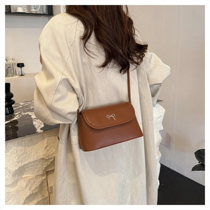 Sac sous le bras marron avec détail de nœud argenté porté par un mannequin