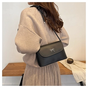 Détail du sac à bandoulière en cuir noir avec un nœud argenté porté par le mannequin