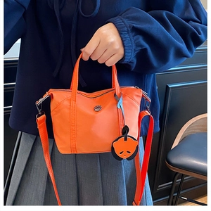 Vibrant orange nylon mini tote bag with panda charm and wide woven strap on a model