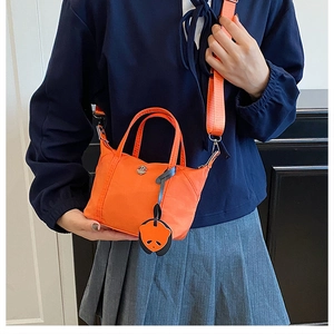 Close-up of orange mini nylon tote bag with shoulder strap and panda charm on a model