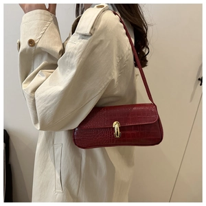 Detailed view of dark red faux crocodile baguette bag with golden metal clasp closure