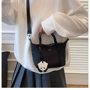 Detailed close-up of a black nylon tote bag with a cute panda pendant on white hoodie