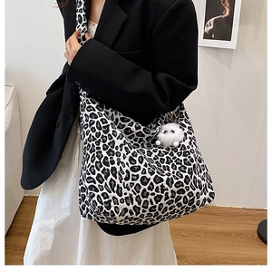 Détail du sac hobo en toile léopard avec pendentif boule en peluche porté à l'épaule