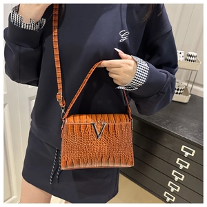 Detail of a brown crocodile-patterned crossbody bag with a silver V-shaped metal buckle