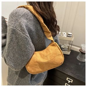 Détail du sac hobo en daim jaune moutarde avec bandoulière plissée et texture douce à l'épaule