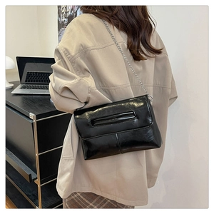 Détail de la pochette enveloppe en cuir verni noir avec chaîne argentée et rabat rainuré