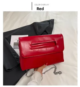 Détail d'un sac enveloppe en cuir PU rouge avec chaîne argentée sur un costume gris
