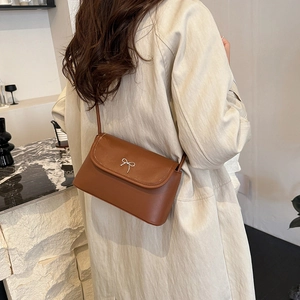 Sac bandoulière marron avec boucle nœud argentée porté par un mannequin dans un cadre pur