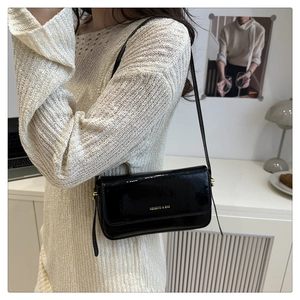 Detail of black patent leather shoulder bag with gold lettering and sleek finish