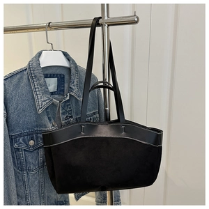 Detail der schwarzen Shopper-Tasche mit Wildledertextur und Kontrastnähten vor Jeansjacke