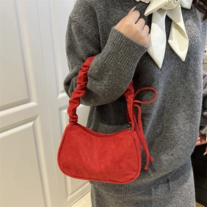 Sac hobo en velours rouge avec anse plissée et détail de nœud sur un pull gris