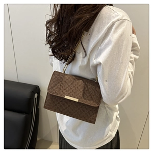 Gros plan sur un sac bandoulière marron tressé avec chaîne dorée et fermoir en métal