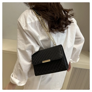 Détail d'un sac bandoulière tressé noir avec chaîne dorée sur un mannequin en blanc