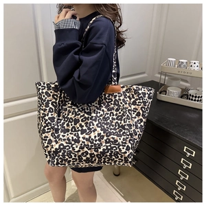 Detailed view of a large leopard print tote bag with brown leather trim on a model shoulder