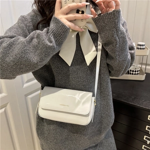 Glossy white patent leather crossbody bag with gold logo in a French minimalist style