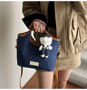 Détail du sac seau en denim bleu avec anses en cuir marron et pendentif ours en peluche