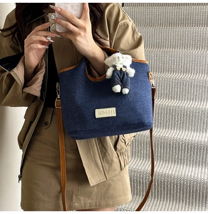 Détail du sac cabas en jean bleu avec garniture en cuir brun et breloque ours mignon