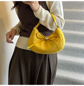 Detail of yellow crescent shoulder bag featuring a decorative bow and heart metal tag