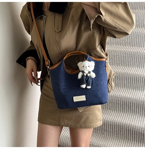 Détail du cabas en denim bleu foncé avec bordure en cuir marron et breloque ours blanc