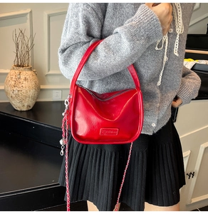 Détail d'un sac à main rouge en cuir verni avec fermeture éclair argentée et chaîne décorative