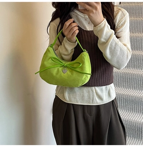 Detail of lime green suede crescent bag with ribbon bow and silver heart pendant