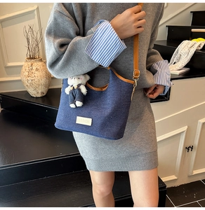 Detail der blauen Denim-Tragetasche mit braunem Lederbesatz und weißem Bärenanhänger