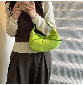 Detail of green suede dumpling bag with bow and silver heart pendant on a model