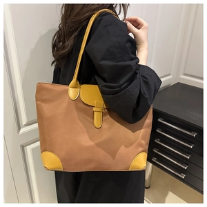 Detail of a brown nylon tote bag with yellow leather flap and handle worn by a model