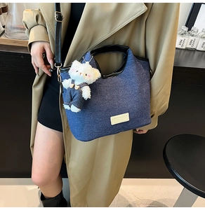 Sac fourre-tout en denim bleu avec bordure en cuir noir et breloque ours sur modèle