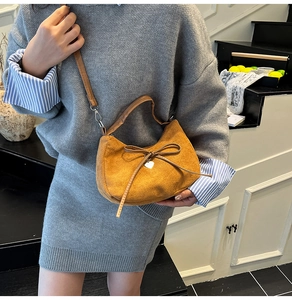Brown vintage suede dumpling bag with bow detail and heart pendant on a model