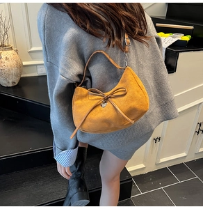 Detail of mustard yellow suede hobo bag with bow and silver heart pendant on model