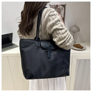 Detailed view of black nylon tote bag with leather buckle and reinforced corners on a model