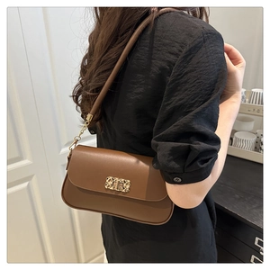 Close-up of a brown leather shoulder bag with a gold metal clasp worn by a model