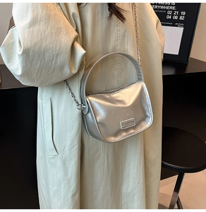 Detalle de bolso plateado con cadena metálica en una modelo con abrigo verde largo