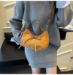 Detail of brown suede handbag featuring a bow tie and heart charm on a gray outfit