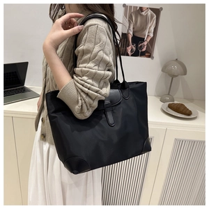 Close-up of black nylon tote bag worn by a model in a cozy indoor minimalist setting