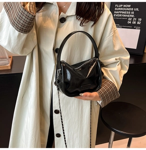 Détail du sac polochon noir brillant avec bandoulière chaîne et poignée sur trench-coat