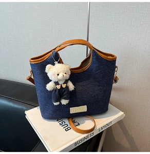 Détail du cabas en denim bleu foncé avec garniture en cuir brun et breloque ours en peluche