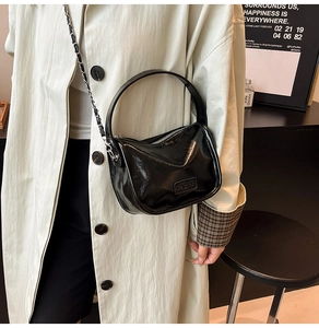 Gros plan du sac en cuir verni noir avec bandoulière chaîne porté par un mannequin