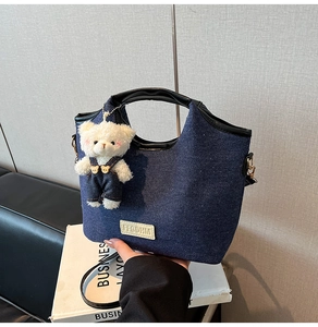 Détail d'un sac seau en denim bleu foncé avec poignée en cuir et charm ours