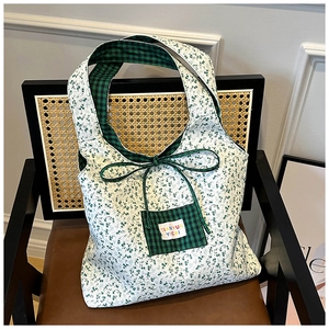 Detail of floral tote bag with green plaid pocket and decorative bow on wicker chair