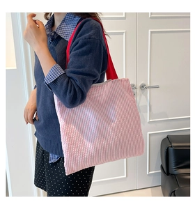 Model wearing a pink striped canvas tote bag with red straps in a minimalist indoor setting