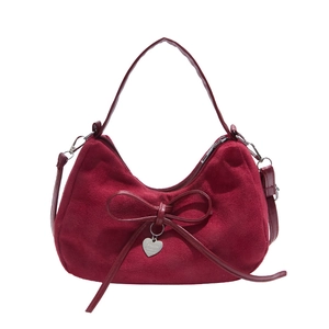 Red suede half-moon handbag featuring a bow detail and a silver heart pendant charm