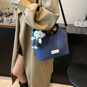 Sac seau en denim bleu avec breloque ours en peluche porté avec un trench-coat kaki