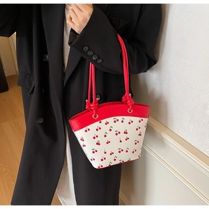 Fashionable cherry print shoulder bag with red handles shown on a model in a blazer