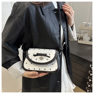 Détail du nœud et du pendentif cœur sur le sac à main blanc texturé porté par le mannequin