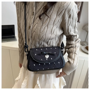Détail d'un sac bandoulière noir avec nœud, pendentif cœur et motifs texturés