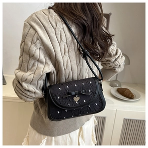 Détail d'un sac bandoulière vintage noir avec motifs lapins et pendentif cœur à nœud